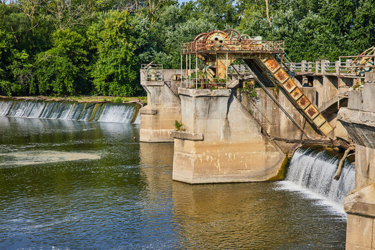 Maumee River Dam with rusty equipment on concrete pillars above waterfalls and forest background in Fort Wayne, IN