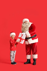 Santa Claus and cute little boy with Christmas gift on red background