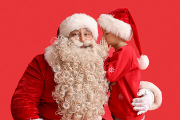 Cute little boy telling wish to Santa Claus on red background