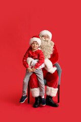Santa Claus and cute little boy on red background