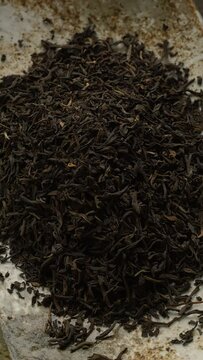 Top view of unpressed pu-erh tea forming a heap on a rectangular ceramic plate. Rustic wooden table. Table spin.  Vertical video.