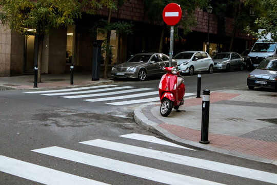 Madrid, Spain. November 19, 2023 Red Piaggio Vespa scooter parked on city street. Eco-friendly vintage retro transportation. European city street. White crosswalk, zebra. Urban landscape. Travel photo