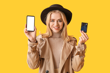 Young woman with modern mobile phone and credit card on yellow background