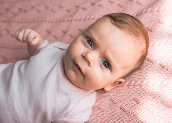 Cute two months old baby infant girl lying on pink blanket and looking at the camera with serious face