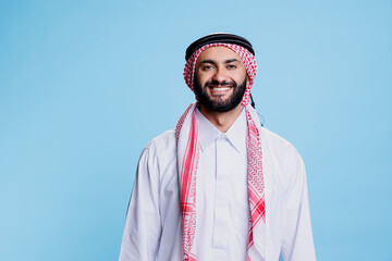 Smiling man dressed in traditional muslim clothes standing with cheerful expression studio portrait. Happy arab person posing in thobe and headscarf while looking at camera with carefree emotion