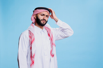 Exhausted muslim man dressed in traditional clothes holding head in pain while suffering from migraine. Tired arab person wearing islamic thobe and headscarf having headache