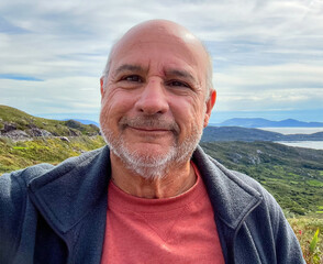Bald, smiling senior with a country side background