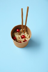 Takeaway box with chinese noodles, Christmas balls and chopsticks on color background