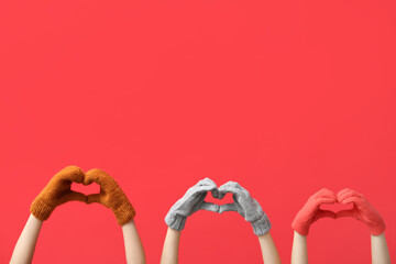 Women in warm gloves holding hands in shape of heart on red background
