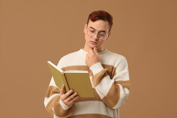 Young man in eyeglasses reading book on color background