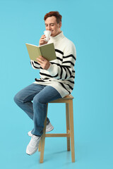 Young man drinking coffee and reading book on color background