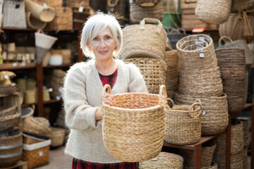 Elderly woman shopper choosing wicker basket in store..
