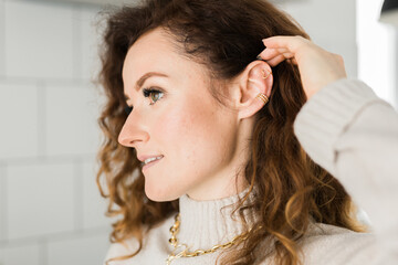Cropped close-up shot of a young woman with two asymmetrical golden ear cuffs. Female with golden...