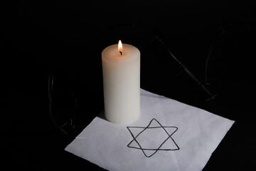 Burning candle with David star and barbed wire on dark background. International Holocaust...