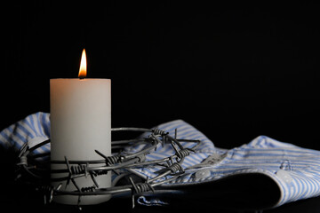 Burning candle with barbed wire and prisoner uniform on dark background, closeup. International...