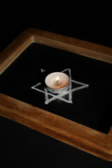 Chalkboard with David star and burning candle on dark background, closeup. International Holocaust...
