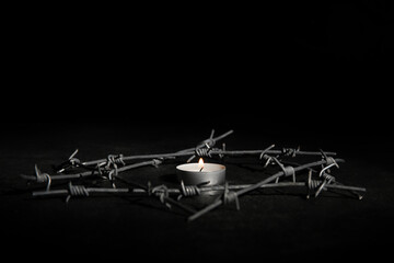 Fototapeta na wymiar Burning candle with barbed wire on dark background. International Holocaust Remembrance Day