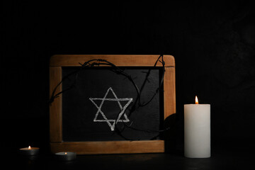 Burning candles with chalkboard and barbed wire on dark background. International Holocaust...