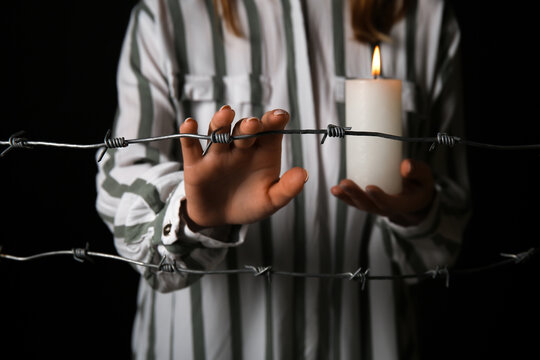 Jewish female prisoner with burning candle behind barbed wire on dark background, closeup. International Holocaust Remembrance Day