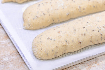Unbaked French baguettes in a bakery. Baguettes made from dough with cereal seeds. Dough for baguettes. Close-up