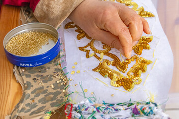 A Tunisian woman embroidering gold sequins onto white cloth.