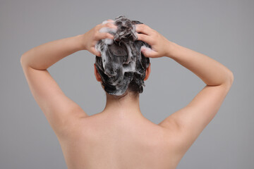Woman washing hair on grey background, back view