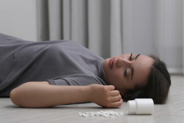 Obraz na płótnie Canvas Depressed woman lying on floor near overturned bottle with antidepressants indoors