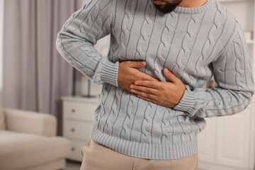 Young man suffering from stomach pain indoors, closeup