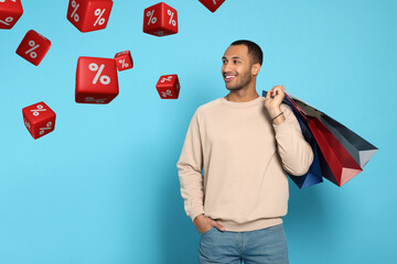 Discount offer. Happy man with paper shopping bags looking at falling cubes with percent signs on...