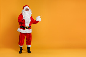 Fototapeta na wymiar Merry Christmas. Santa Claus pointing at something on orange background, space for text