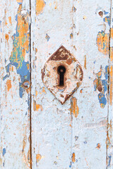 A keyhole on an old door with peeling paint.