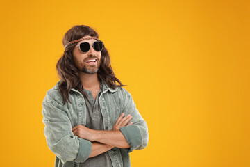 Stylish hippie man in sunglasses on orange background, space for text