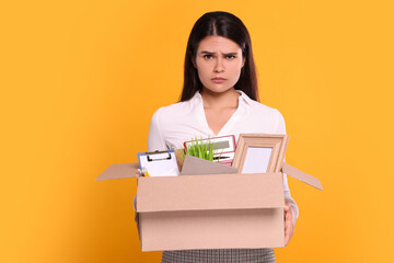 Upset unemployed woman with box of personal office belongings on orange background