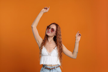 Stylish young hippie woman in sunglasses dancing on orange background