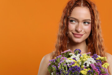 Beautiful young hippie woman with bouquet of colorful flowers on orange background, space for text