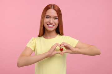 Beautiful happy woman making heart with her hands on pink background