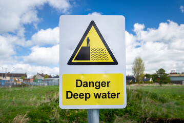 Danger Deep Water warning sign close up by rural waterway river stream. 