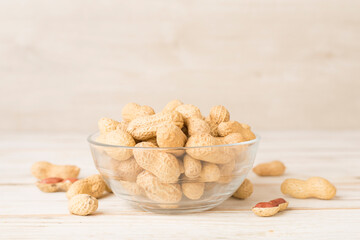 Unpeeled peanuts in bowl on wooden table