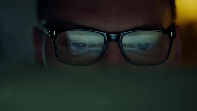IT programmer, a man with glasses, works at night with a portable laptop. His face expresses seriousness as he carefully studies the information on the screen. Scores reflect the changing data picture