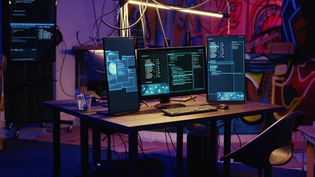 Jib down shot of advanced technology computer system running malicious code in empty warehouse. PC monitors in empty graffiti painted underground hideout used by hackers to commit illicit activities