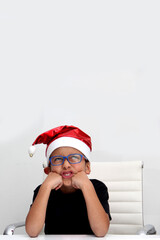 Obraz premium 7-year-old dark-skinned Latino boy with a Santa Claus Christmas hat looks sad and angry because he doesn't like the holidays and they didn't give him what he wanted