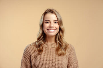 Portrait of smiling attractive young woman wearing stylish warm winter sweater looking at camera standing isolated on beige background. Concept of natural beauty - obrazy, fototapety, plakaty