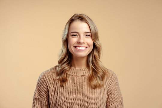 Portrait Of Smiling Attractive Young Woman Wearing Stylish Warm Winter Sweater Looking At Camera Standing Isolated On Beige Background. Concept Of Natural Beauty