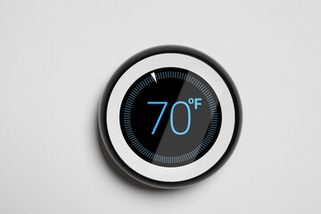 Thermostat displaying temperature in Fahrenheit scale. Smart home device on white wall