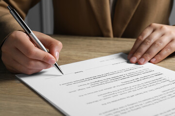 Woman signing document with pen at wooden table, closeup