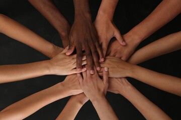 Group of multiracial people joining hands together on black background, closeup - obrazy, fototapety, plakaty