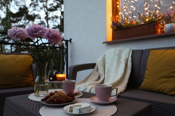 Rattan table with drink, food and flowers on outdoor terrace in evening