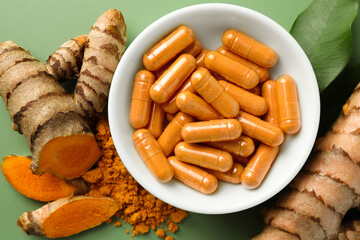 Aromatic turmeric powder, pills and raw roots on green background, flat lay