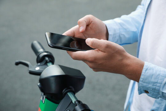 Man using smartphone to pay and unblock electric kick scooter outdoors, closeup