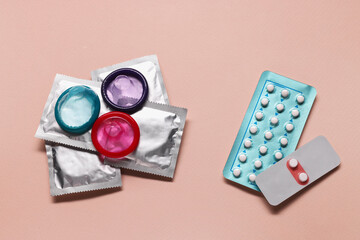 Birth control pills and condoms on pink background, flat lay. Choosing method of contraception